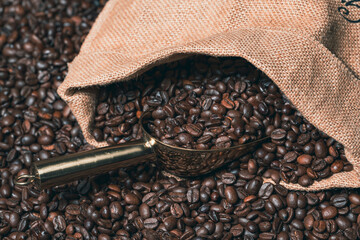 Jute sack full of coffee with a golden coffee scoop on a background of coffee beans