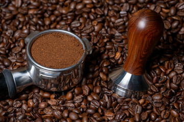Coffee amper and a coffee portafilter filled with freshly ground coffee on a bed of many coffee beans