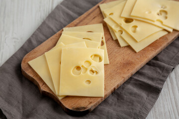 Slices of Maasdam cheese on a wooden board, side view.