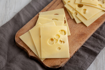 Slices of Maasdam cheese on a wooden board, side view.