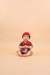 A little boy wearing a bright red Asian national costume against a cream background.