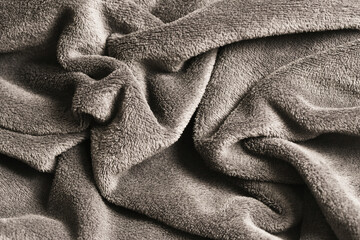 Fototapeta premium Soft, crumpled grey blanket with wavy texture. Closeup of plush, wrinkled fabric with shadows. Cozy cotton textile background.