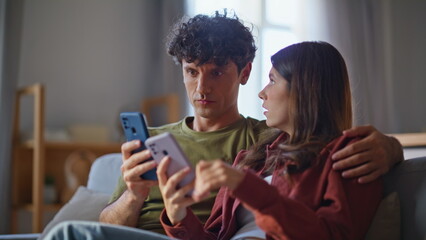 Talking couple holding smartphones sitting sofa closeup. Lovely spouses relaxing