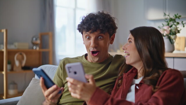 Amazed winners watching smartphones reacting success at room together closeup