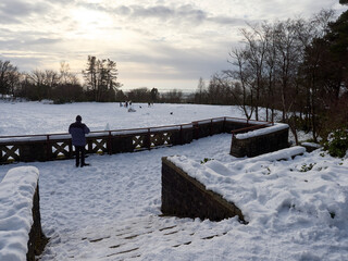 Rivington Terraced Gardens. Lone figure in winter coat observes snowy landscape at sunset.