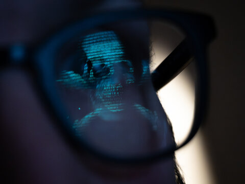 An hackers ASCII skull and crossbones image reflected in the lens of a pair of glasses