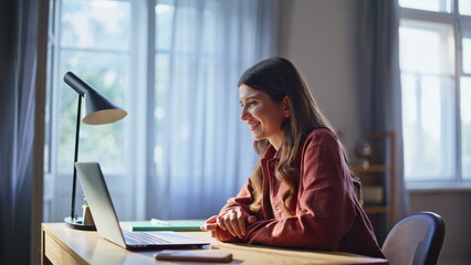 Girl video calling laptop at cozy living room. Happy woman waving hand at home