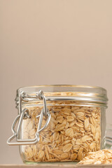 Rolled oats in a glass jar with a metal clasp on a neutral background, promoting sustainable and...