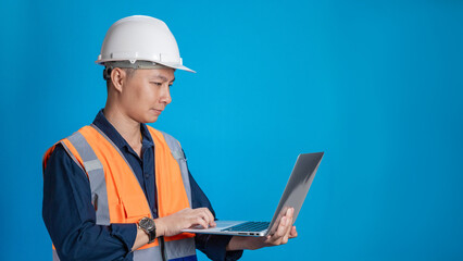Confident young engineer wearing orange and a safety helmet stands holding a laptop, phone with various emotions.