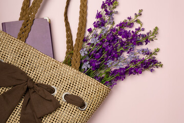 Book and flowers in a straw bag on pink background . Flat lay, top view.