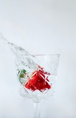 
A crystal-clear glass captures the energy of a splash, highlighting a vibrant red strawberry and green mint leaves. The frozen motion and clean background create a striki