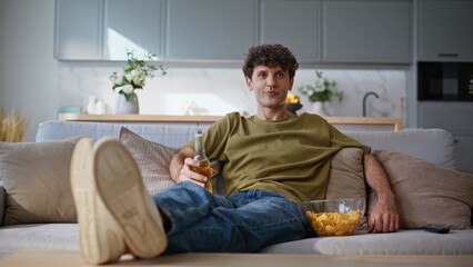 Relaxed man watching show tv resting at home weekend. Smiling guy drinking beer