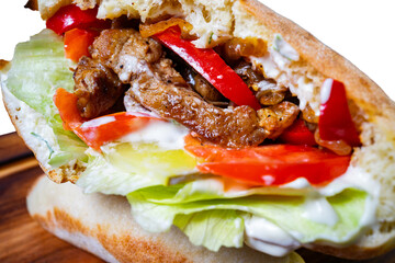 Savory sandwich filled with grilled vegetables and sauce on a wooden surface