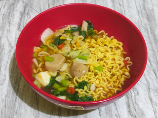 A bowl of Indonesian noodle soup with vegetables and meatball pieces.