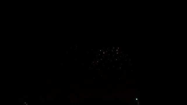 gold red blue sparks scattering fireworks on the black night sky over the city. General plan