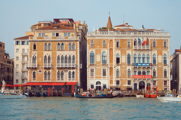A scenic view of historic Venetian buildings along the Grand Canal, featuring gondolas and water traffic in a vibrant waterfront setting. Perfect for travel and cultural imagery. 