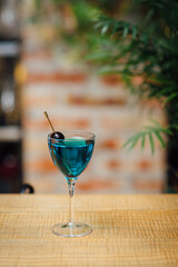 Aviation cocktail in a martini glass, garnished with a black cherry, captured in close-up. Shot with shallow depth of field, natural light, wooden table, and blurred brick background, vertical image