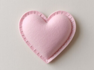 Pink felt heart with stitching on light background.