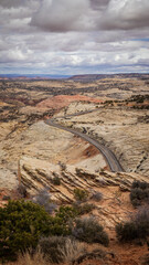 A winding road in Utah stretches through a breathtaking rocky landscape, with sharp turns and steep inclines. The view reveals the contrast between the asphalt and the reddish hues of sandstone cliffs