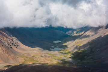 Aerial top view to green rocky hilly valley with two turquoise lakes under lush low clouds. Most...