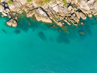Clear turquoise water reveals rocky seabed along a coastal shoreline during a sunny day