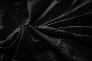 Fototapeta premium Draped dark fabric with soft folds and shadows creating a moody, textured background.