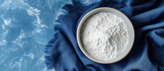 White powder in a bowl on blue cloth surface with textured background and copy space for text insertion