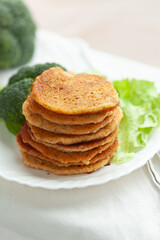 A stack of savory pancakes, golden brown and crispy, served on a white plate with fresh broccoli and lettuce.