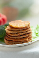 Stack of golden-brown pancakes on a plate, alongside fresh vegetables.