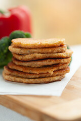 A stack of golden-brown, savory pancakes on a wooden board, with blurred vegetables in the background.  A delicious and healthy-looking meal.
