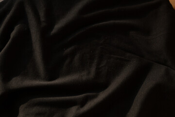 Close-up of dark fabric texture. Soft, draped material with subtle folds and shadows creating a...