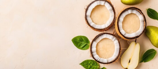 Fresh coconut halves with light brown flesh arranged beside green pears and leaves on a neutral background with Copy Space.