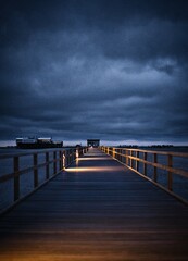 Obraz premium Ein beleuchteter Pier in der blauen Stunde führt zur Nordsee, während das sanfte Licht der Lampen eine magische Atmosphäre schafft und die Schönheit der Küstenlandschaft unterstreicht.