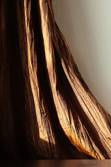 Textured fabric drapes dramatically, catching the light in rich bronze and brown hues.  A...