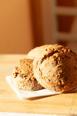 Three freshly baked brown bread rolls on a wooden surface, bathed in warm sunlight.