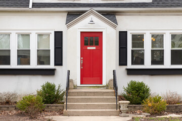 A red front door detail on a white home with concrete steps and iron railings leading up to the door.