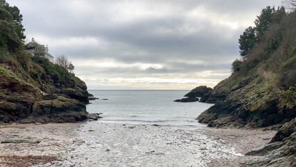 Secluded coastal Mill Bay with rugged cliffs, a rocky shoreline, and a calm ocean view under an overcast sky, offering a peaceful and serene atmosphere - Kingswear, Devon, UK