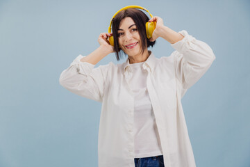Happy mature woman listening music with yellow headphones on blue background