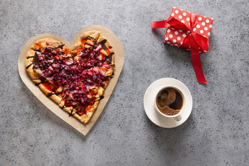 Food for Valentine's Day. Romantic heart shaped sweet homemade pizza, gift and coffee on gray background. View from above.