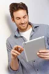 Happy white man working using tablet computer leaning against white wall. © nyul