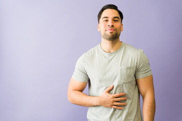Young man holding his stomach feeling full or bloated after eating