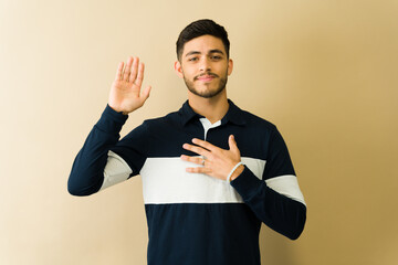 Serious Latin man taking an oath with hand on chest and raised hand