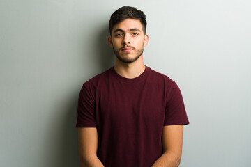 Young man posing with serious expression against gray wall