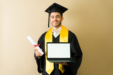 Happy graduate showing laptop and diploma at graduation ceremony