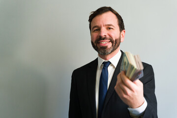 Smiling businessman showing wad of cash money in a studio
