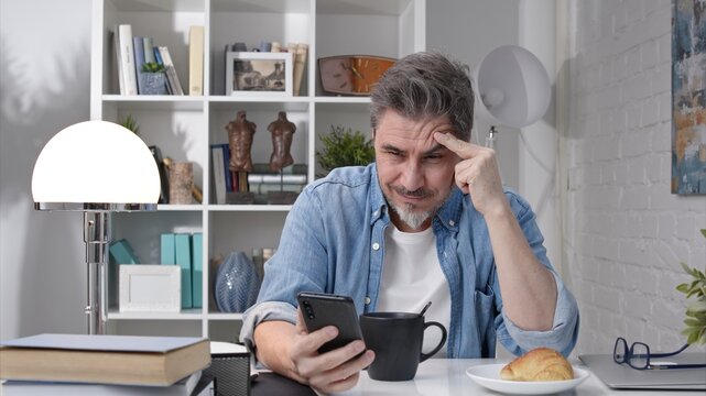 50s man having breakfast checking news on phone drinking morning coffee at home. Confident happy smiling.