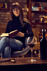 young woman drinking wine at loft home while reading a book.