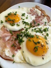 Fried eggs with ham and chives on white plate