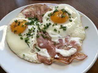 Sunny side up eggs with ham and chives on white plate