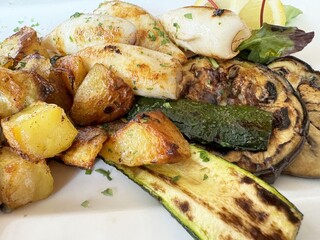 Grilled vegetables and roasted potatoes with calamari garnished with herbs